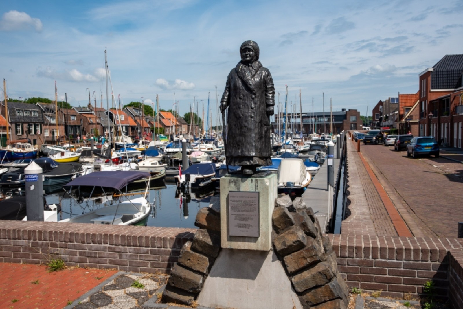 Bronzen standbeeld van vissersvrouw in klederdracht met de Spakenburgse museumhaven op de achtergrond